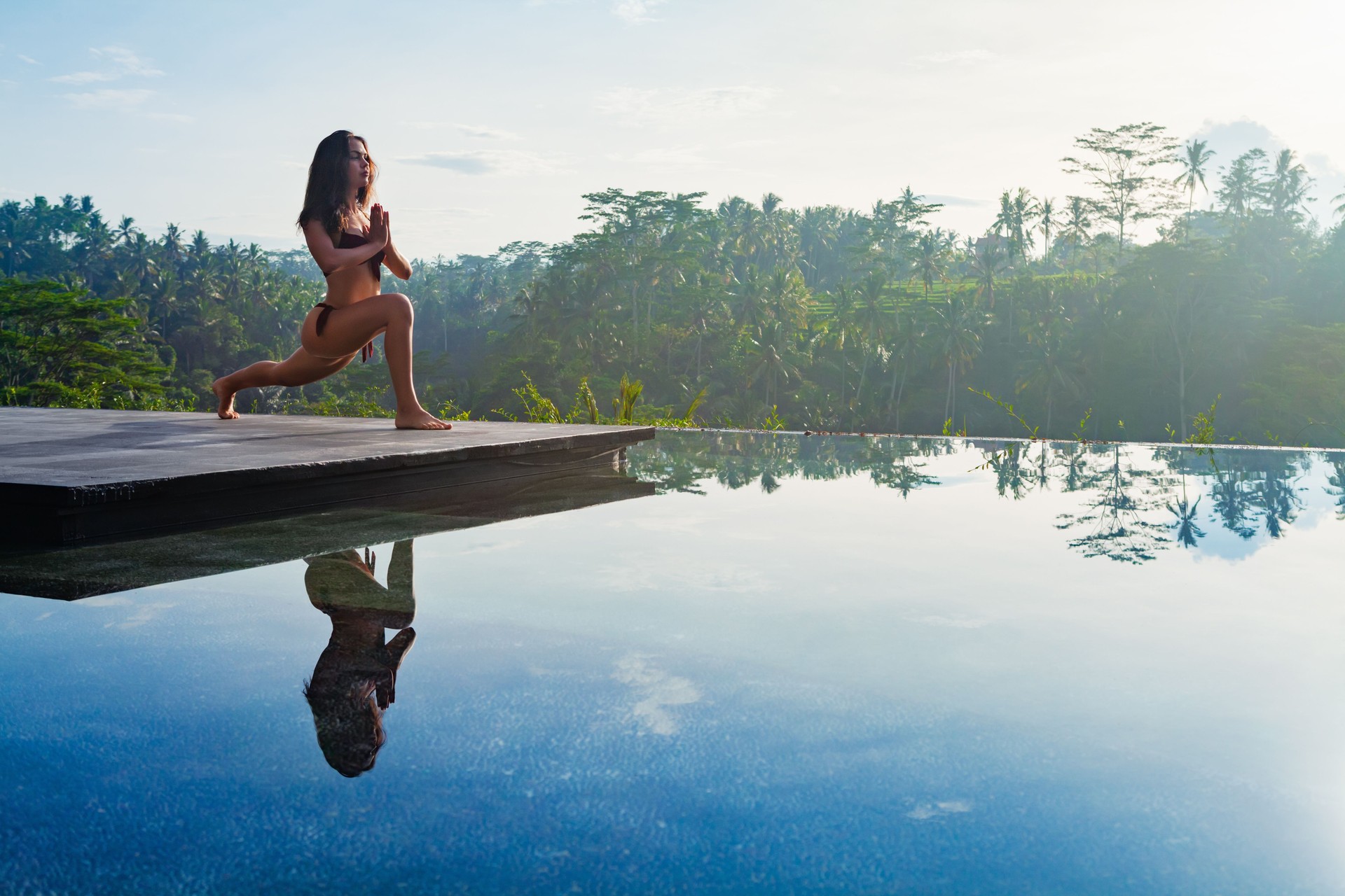 Yoga meditating at infinity pool on sunrise I tropical jungle